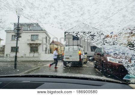 Silhouette of woman crossing street on a snowy day - senn by the driver point ov view personal perspective through wet windshield window