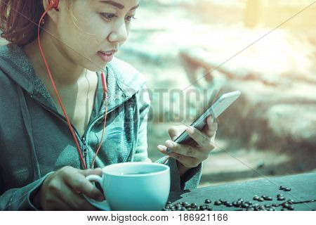Women drink coffee Play mobile phone On the wooden table floor there is a coffee bean.