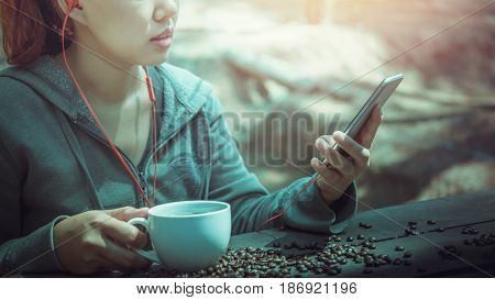 Women drink coffee Play mobile phone On the wooden table floor there is a coffee bean.