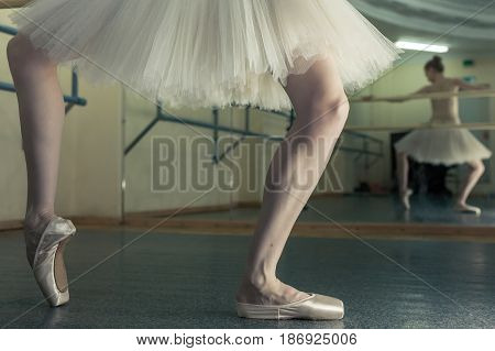 Ballet dancer in a pointe and a pack squats at the bench. Reflection in the mirror in the ballet class. Classical ballet. Prima ballerina. Shooting close-up.