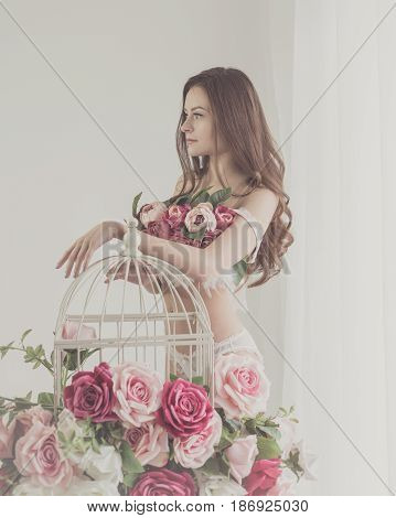 Lovely girl in underwear. Bra of flowers. Spring mood. She stands by the empty cage near the window. Soft focus.