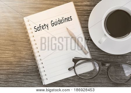 Safety Guidelines text written on a notebook with glasses pencil and coffee cup on wooden table.