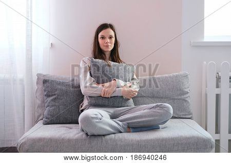 Lonely depressed woman at home, she is sitting on the sofa and hugging a pillow
