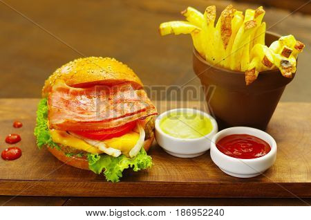Delicious bakon hamburger with ketchup, mustard and french fries on wooden board..