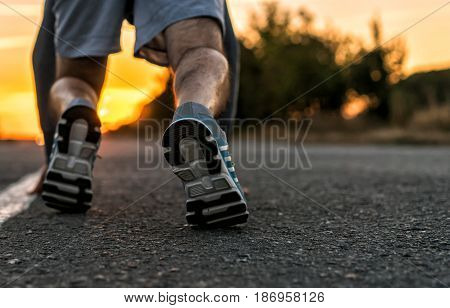 Runner feet running on road closeup on shoe. man fitness sunet jog workout welness concept on sunrise.