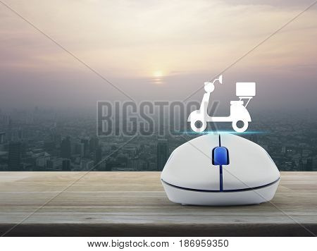 Motor bike icon with wireless computer mouse on wooden table over modern city tower at sunset vintage style Business internet delivery service concept