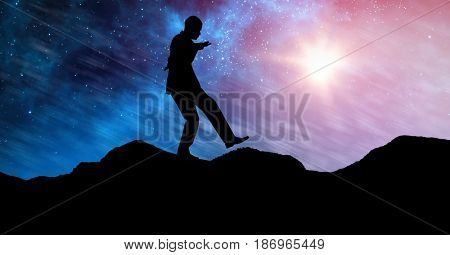 Digital composite of Silhouette businessman balancing on mountain against sky at night