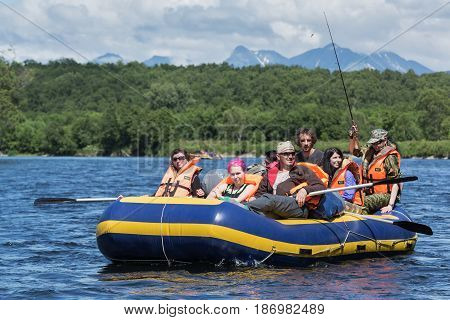 BYSTRAYA RIVER KAMCHATKA PENINSULA RUSSIA - JULY 13 2016: Summer rafting on Kamchatka - group of tourists and travelers floating on calm river on raft on background of green forest and mountains.