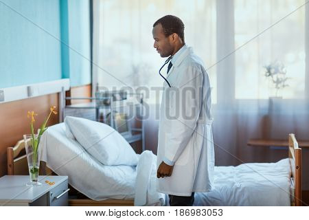 Side View Of Doctor Standing Near Hospital Bed And Looking At Flowers In Vase