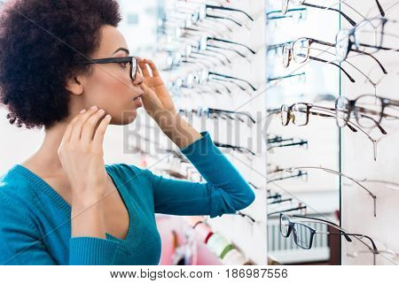 Black woman trying on glasses she wants to buy in optician store