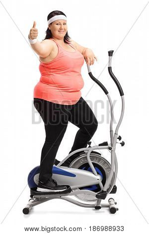 Full length portrait of an overweight woman exercising on a cross trainer machine and making a thumb up sign isolated on white background