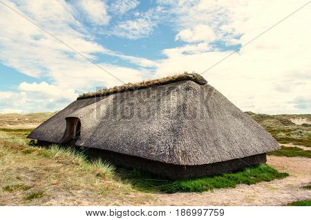 cottage with thatched roof and clouds in the background