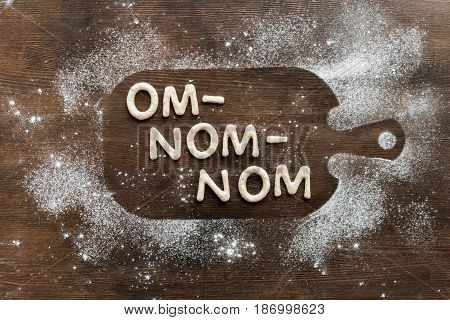 Top View Of Edible Lettering Om-nom-nom Made From Cookies On Wooden Cutting Board, Baking Cookies Co