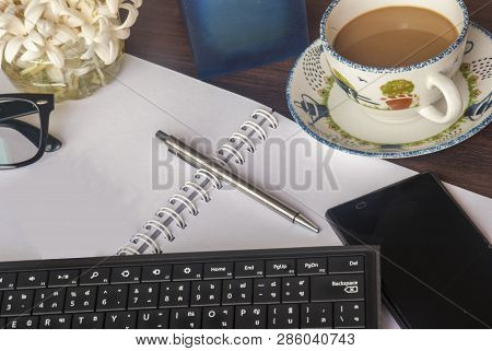 Keyboard, Note Book, Pen, Mobile Phone, Glasses, Scented Candles, Flowers And Coffee On A Brown Wood