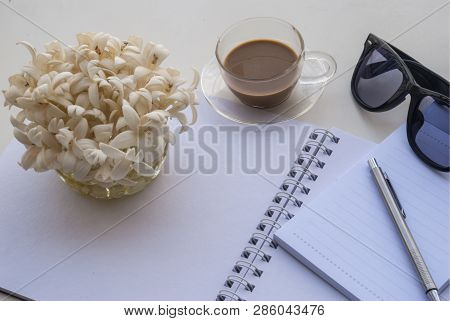 Flowers, Glasses Pens And Coffee Mugs On A White Note Book