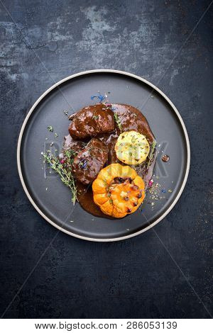Traditional German braised pork cheeks in brown red wine sauce with fried mushed potatoes and pumpkin as top view on a modern design plate with copy space 