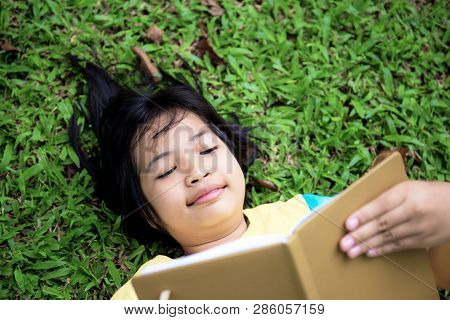 Asian Girl Are Reading A Book On Lawn In Park.