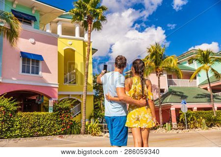 Couple on winter vacation taking pictures of pastel colored beach houses cottages in tropical holiday destination Fort Myers, Florida. Man tourist taking picture with phone.