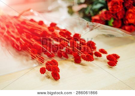 Beautiful Fresh Red Flowers Lying On The Light Wooden Table Near The Red Roses. Bouguet Of Exotic Fl