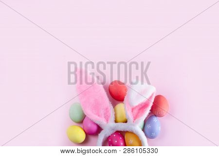 Easter Rabbit Flaffy Ears And Colored Easter Colored Eggs On Pink Background, Top View With Copy Spa