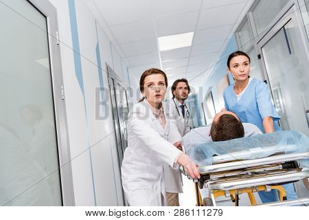 Worried Doctors And Nurse Transporting Unconscious Patient On Gurney