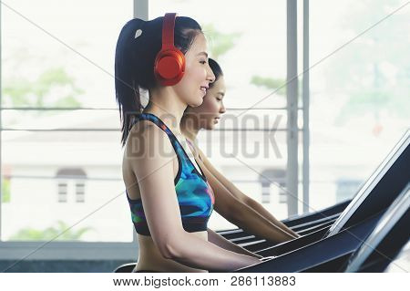 Side View Of Two Attractive Sports Women Littening To Music On Running Track. Girls On Treadmill.