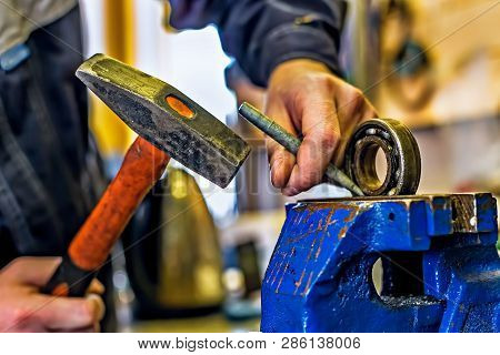 A Mechanic With A Hammer And A Chisel Works Behind A Workbench.