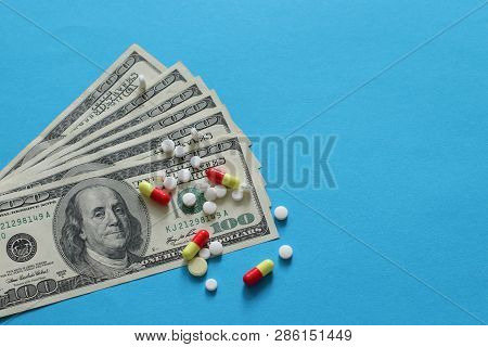 Scattered Pharmaceutical Medicine Pills, Tablets And Capsules On Dollar Money Isolated On Blue Backg