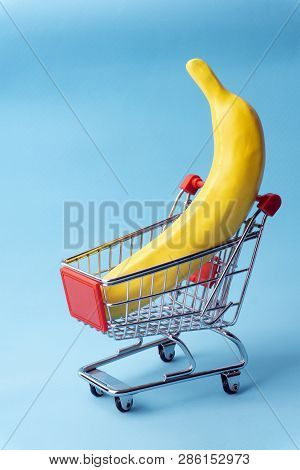 Shopping Minimal Concept. Banana In A Toy Shopping Cart. Minimal Pop Art Background, Contemporary Ar