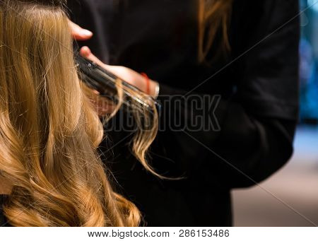 Close Up Of Pretty Young Woman Is Getting Her Hair Equalized In Beauty Salon. The Hairdresser Is Com