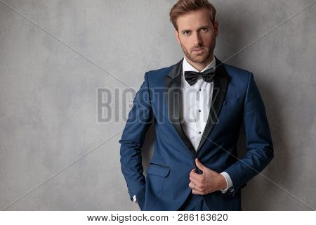 Ellegant man buttoning his jacket with a hand in his pocket on a light grey background