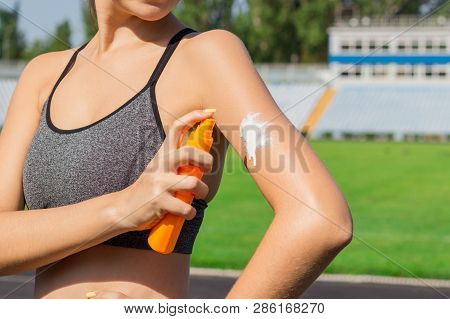 Young Female Runner Standing And Putting Sun Lotion On Hand. Girl Using Sunscream Before Sport Runni