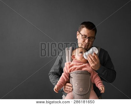 Fathre And His Kid In Baby Carrier At The Grey Background Wall, Baby Wearing Concept
