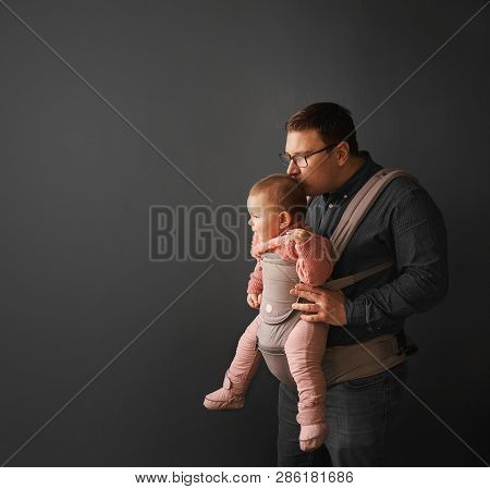 Fathre And His Kid In Baby Carrier At The Grey Background Wall, Baby Wearing Concept