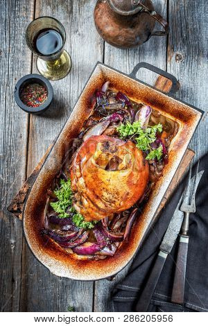 Traditional Bavarian schweinshaxe with onion as top view in a rustic stewpot on an old wooden board 