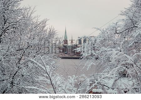 Stockholm City And Two Church Towers Seen Through The Woods On The Other Side Of The River On A Wint