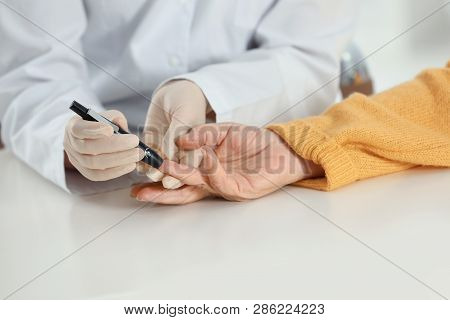 Doctor Taking Patient's Blood Sample With Lancet Pen In Hospital, Closeup. Diabetes Control
