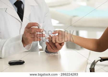 Doctor Taking Patient's Blood Sample With Lancet Pen In Hospital, Closeup. Diabetes Control