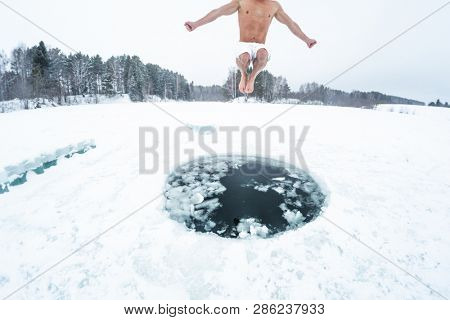 Young man jumps and flies into the ice hole made on the winter lake