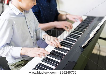 Midsection Of Boy Learning To Play Electric Piano From Teacher In Music Class