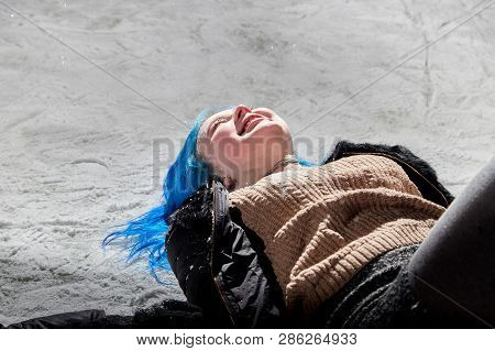 Girl With Blut Hair Lying On The Snow Of A Ice Arena In The Evening City Square In Winter