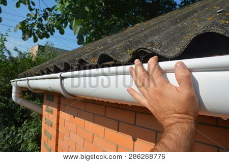 House Asbestos Roof With Plastic Roof Gutter Pipe Repair. Contractor Hand Repair House Roof Gutter.