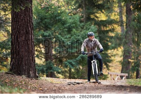 A Senior Man With Electrobike Cycling Outdoors On A Road In Park In Autumn.