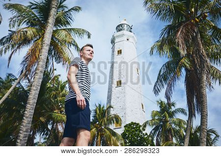 Young Man Looking Away Under Palm Trees Against Lighthouse. Coastline In Sri Lanka.