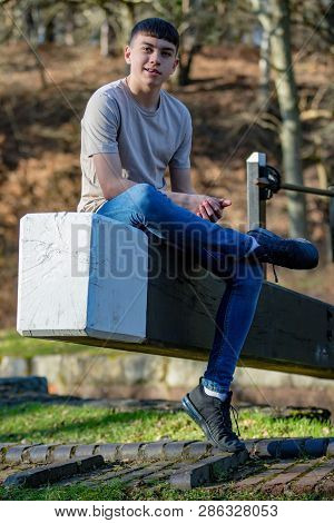 Portrait Of A Caucasian Teenage Boy On A Warm Spring Day Sitting On A Lock Gate