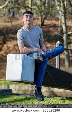 Portrait Of A Caucasian Teenage Boy On A Warm Spring Day Sitting On A Lock Gate
