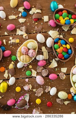 easter, sweets and confectionery concept - chocolate eggs and candy drops on wooden table