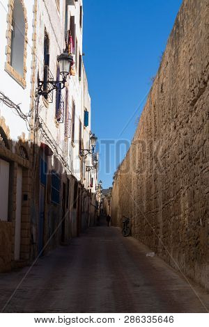 Street With A New Pavement. Traditional White Residential Houses On The Left Side, High Stone Wall O