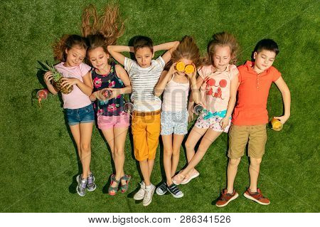 Group Of Happy Children Playing Outdoors. Kids Having Fun In Spring Park. Friends Lying On Green Gra