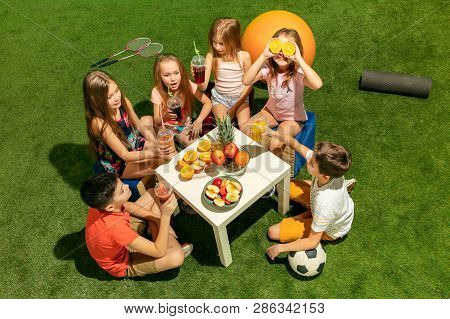Kids Fashion Concept. The Group Of Teen Boys And Girls Sitting On Green Grass At Park. Children Colo